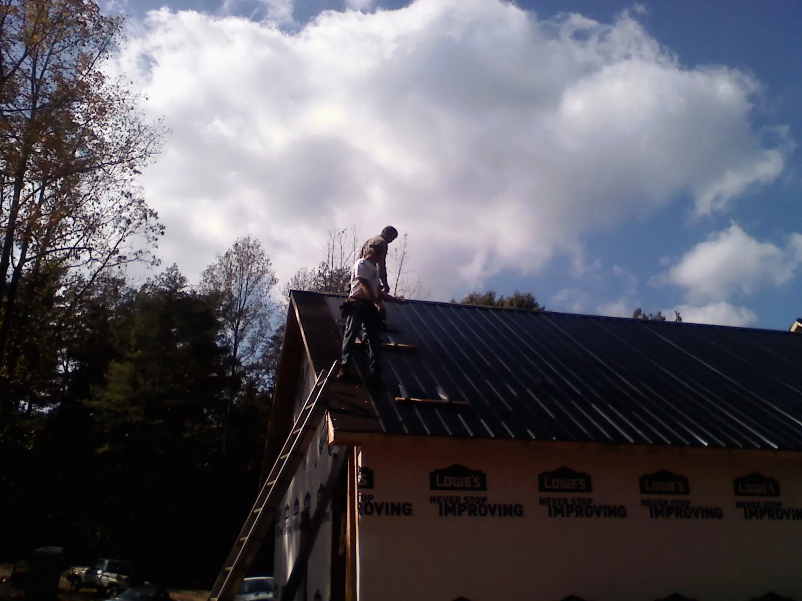 Roofer fastening dark metal panels high against a cloudy sky, from a Roof Inspection job in Arcadia
